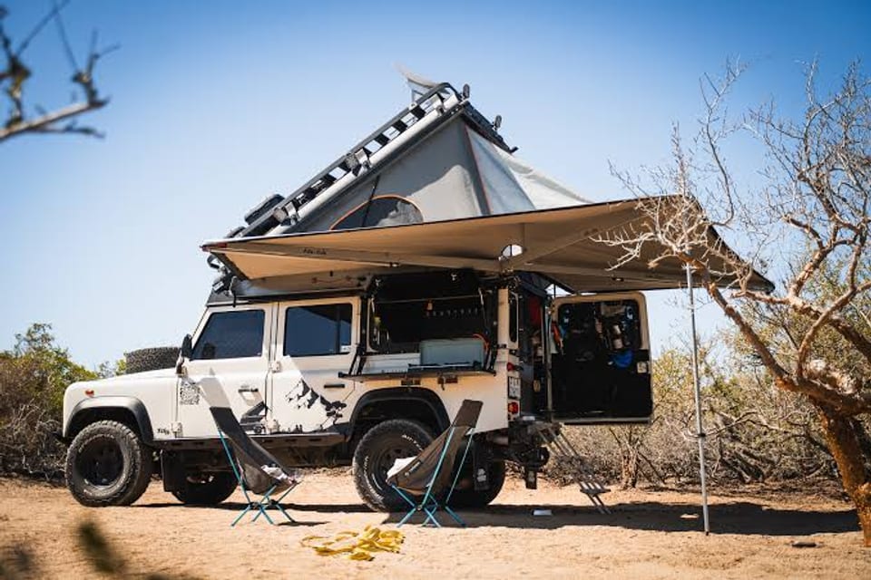 A kitted expedition Land Rover Defender with a rooftop tent and awning at a remote camp.