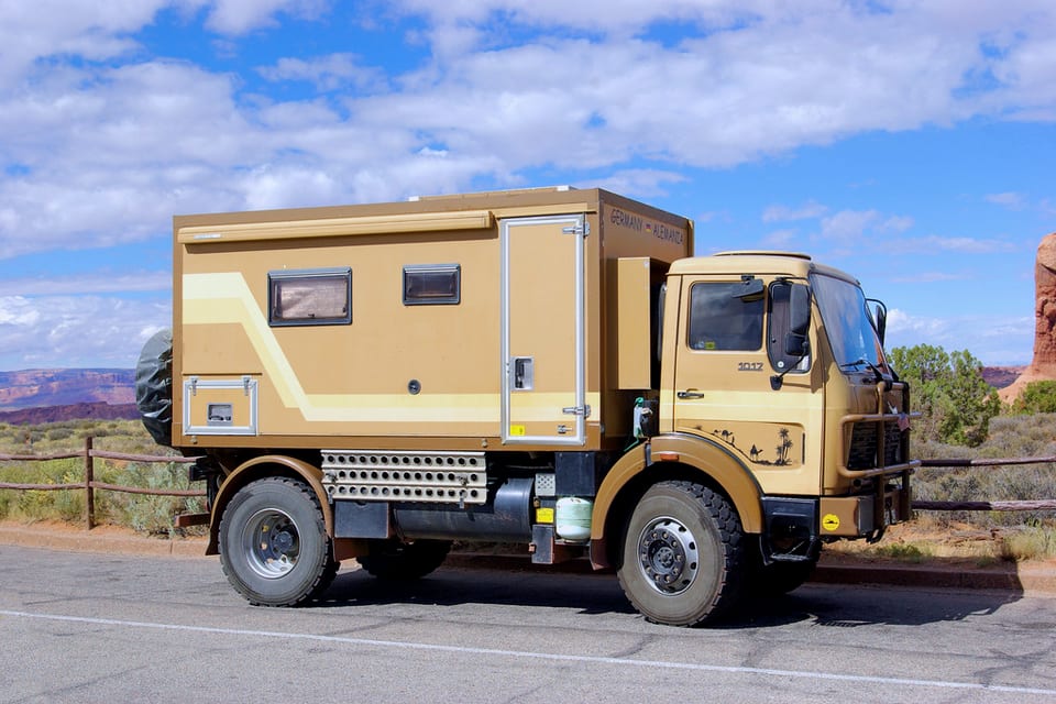 A four-wheel-drive expedition truck with a camper body on a desert road.