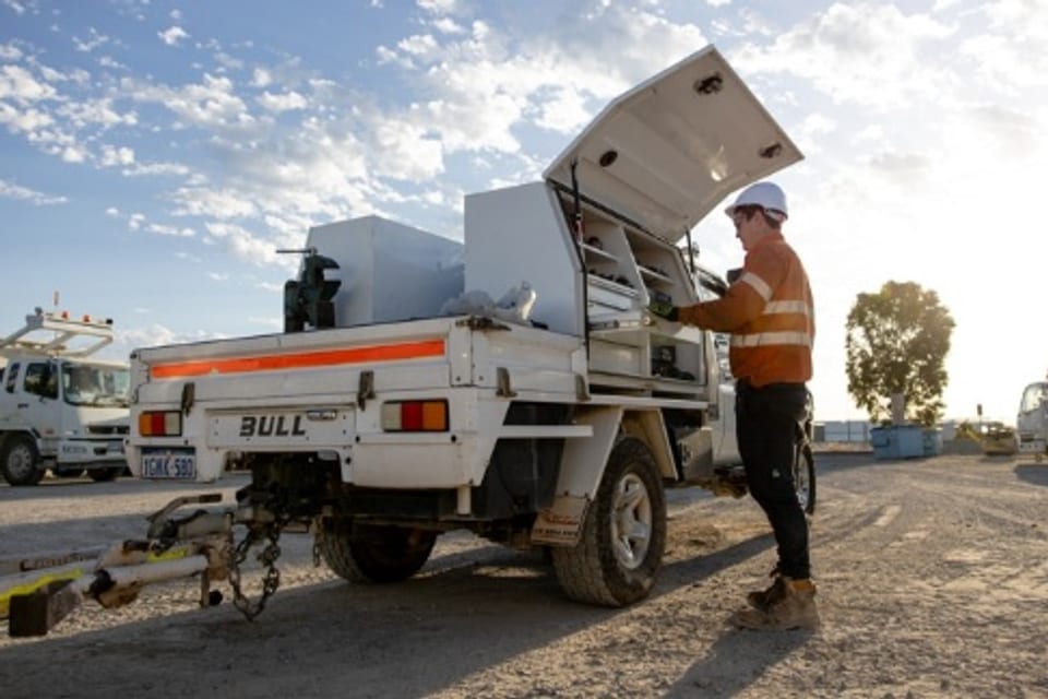 A technician in hi-vis working from the equipped load bay of a white field-service bakkie on a worksite.